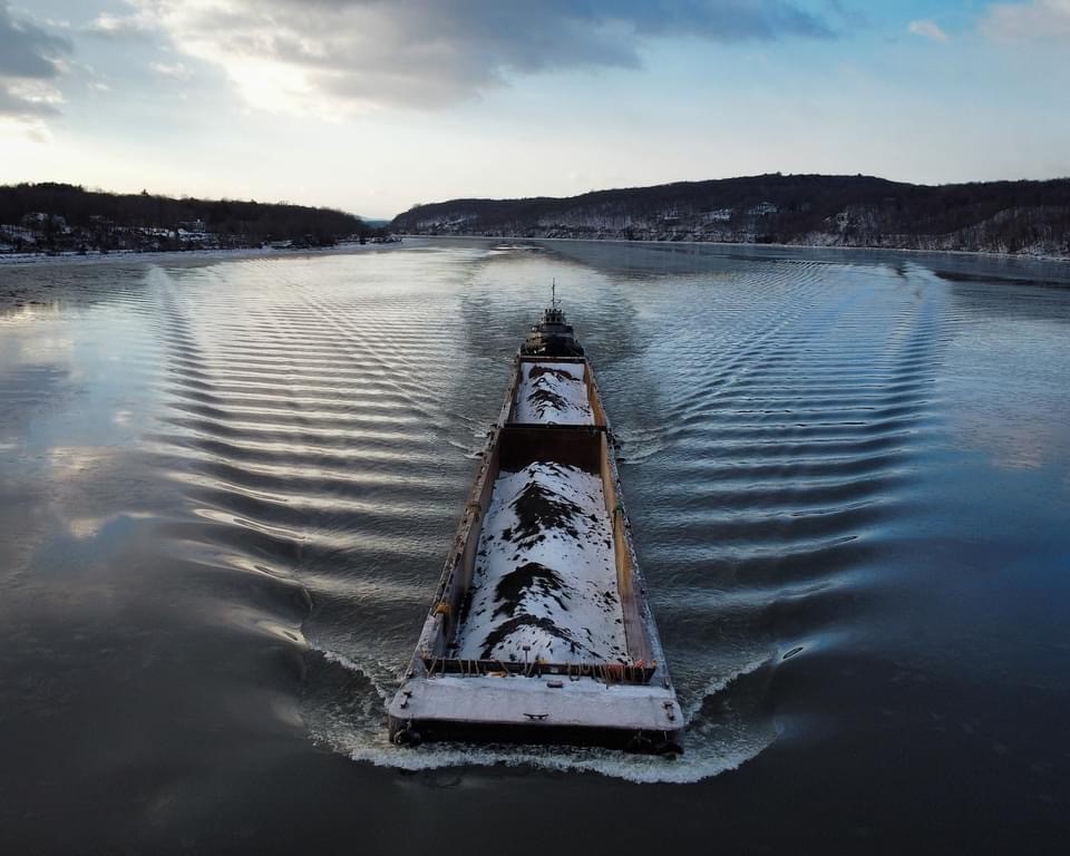 Barge loaded with cargo moving down a winter river, viewed from above